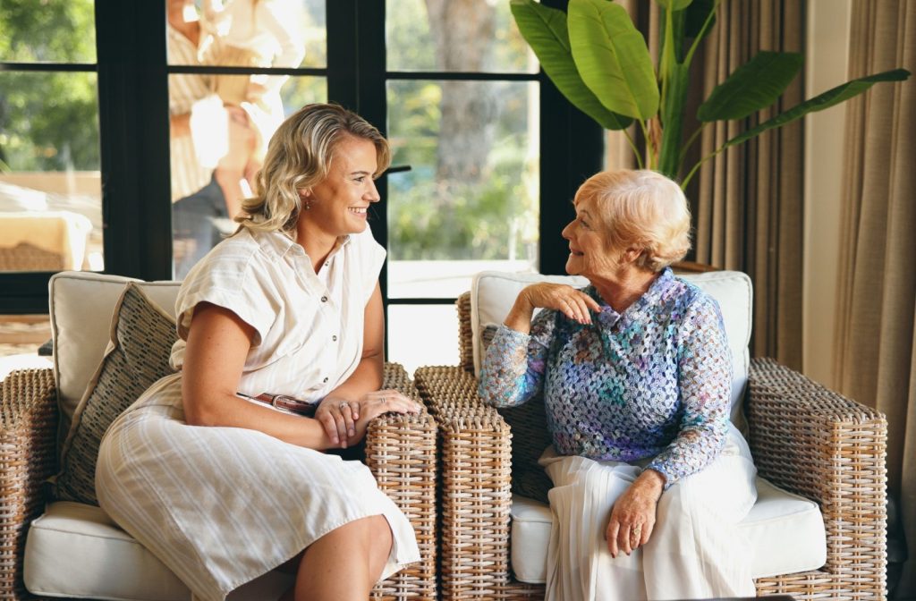 A senior and their adult child smiling while seated in a cozy lounge setting sharing a warm conversation in a senior living community