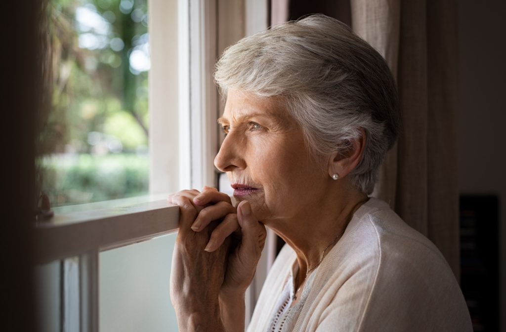 An older adult with memory loss looks out their kitchen window, confused