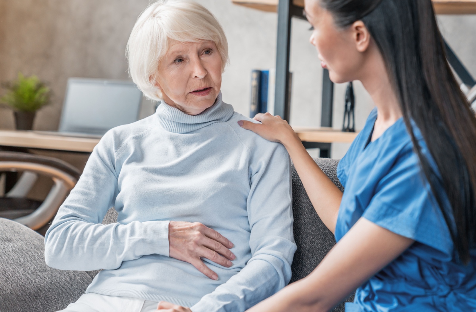A caregiver checks in on a seated resident in memory care and touches their arm to show support
