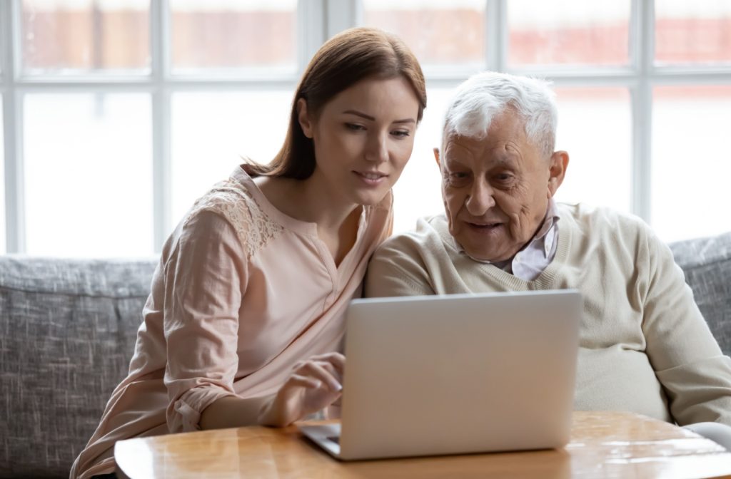 An adult and their senior parent search the internet for assisted living communities while sitting on a sofa together.