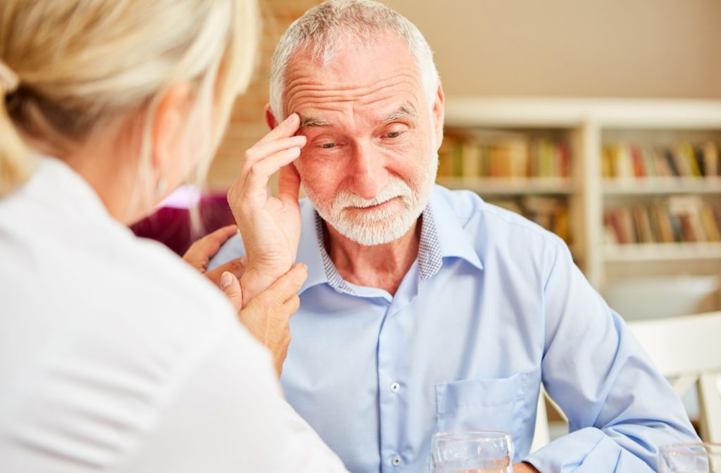 A senior touches their temple with an upset expression while speaking to their adult child.