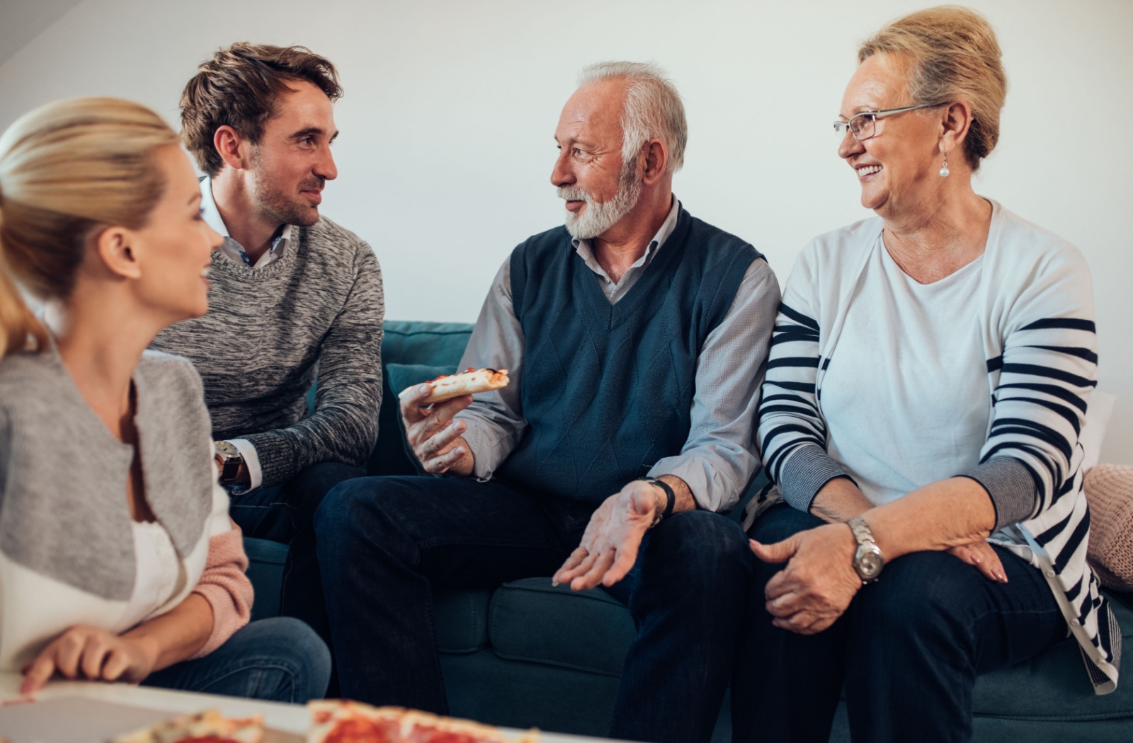 Two adult child siblings spend time with their senior parents while eating pizza.
